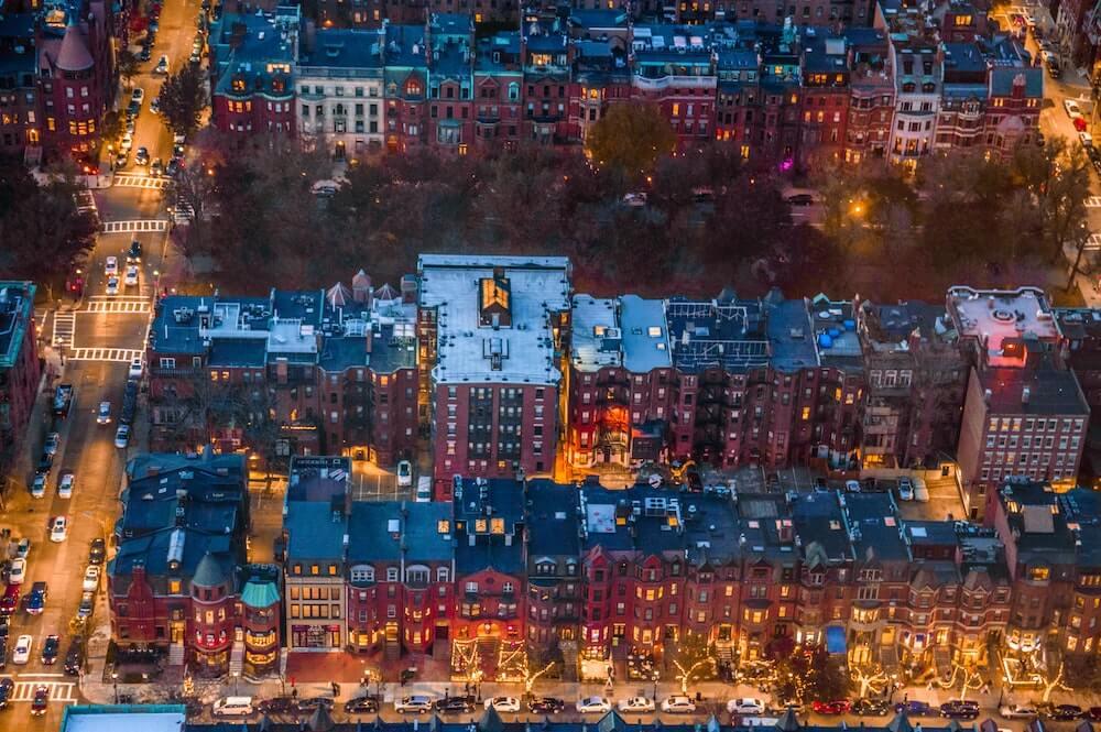 An aerial view of downtown Boston, Massachusetts at night with buildings using electricity to keep all of their lights on.