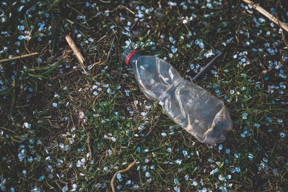 A plastic water bottle laying in the grass with little broken pieces of plastic around it.