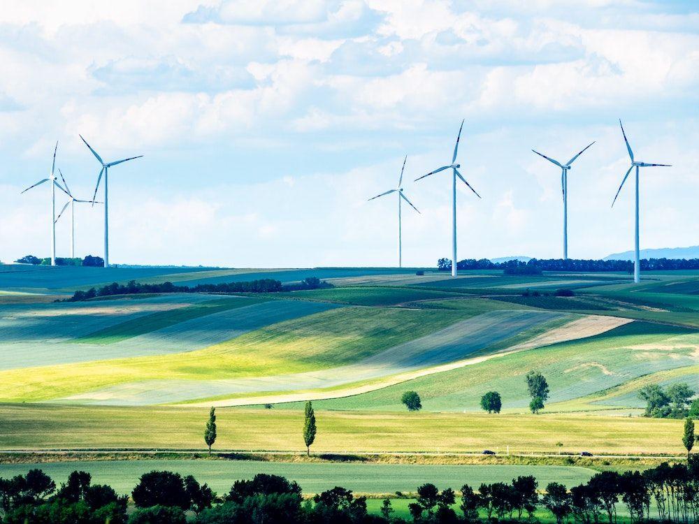 Multiple wind turbines on rolling green farmland.