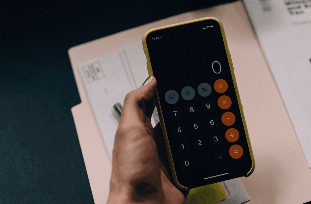 A hand holding an iPhone with the calculator app showing and paperwork on the table.