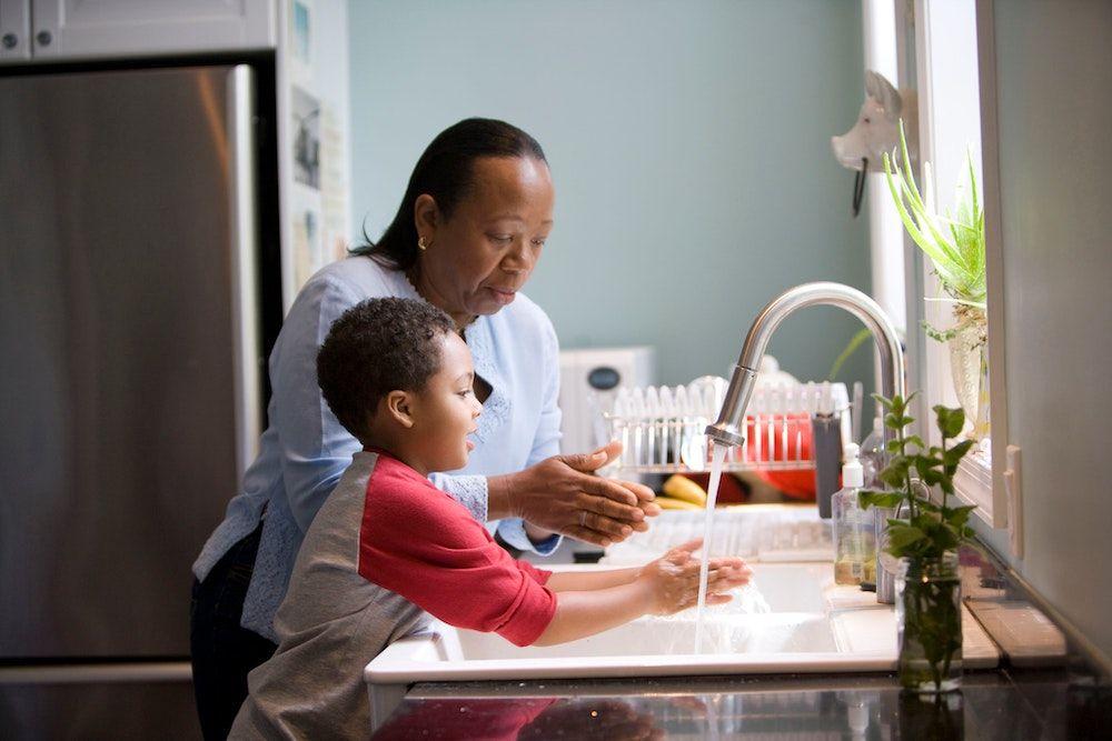A mother and her toddler son stand at the kitchen sink, washing their hands.