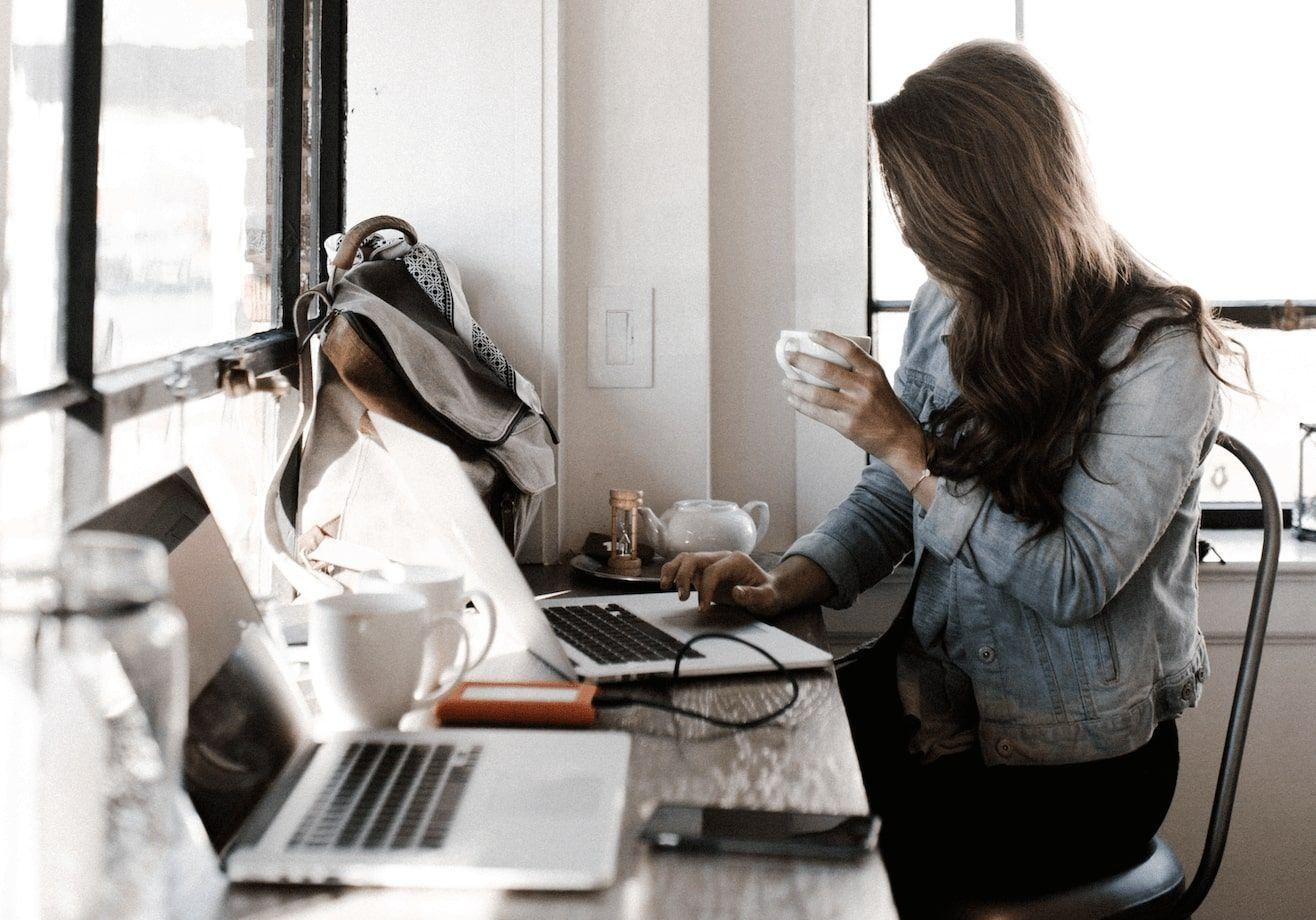 A woman sitting at her kitchen table, drinking coffee, working on her computer.
